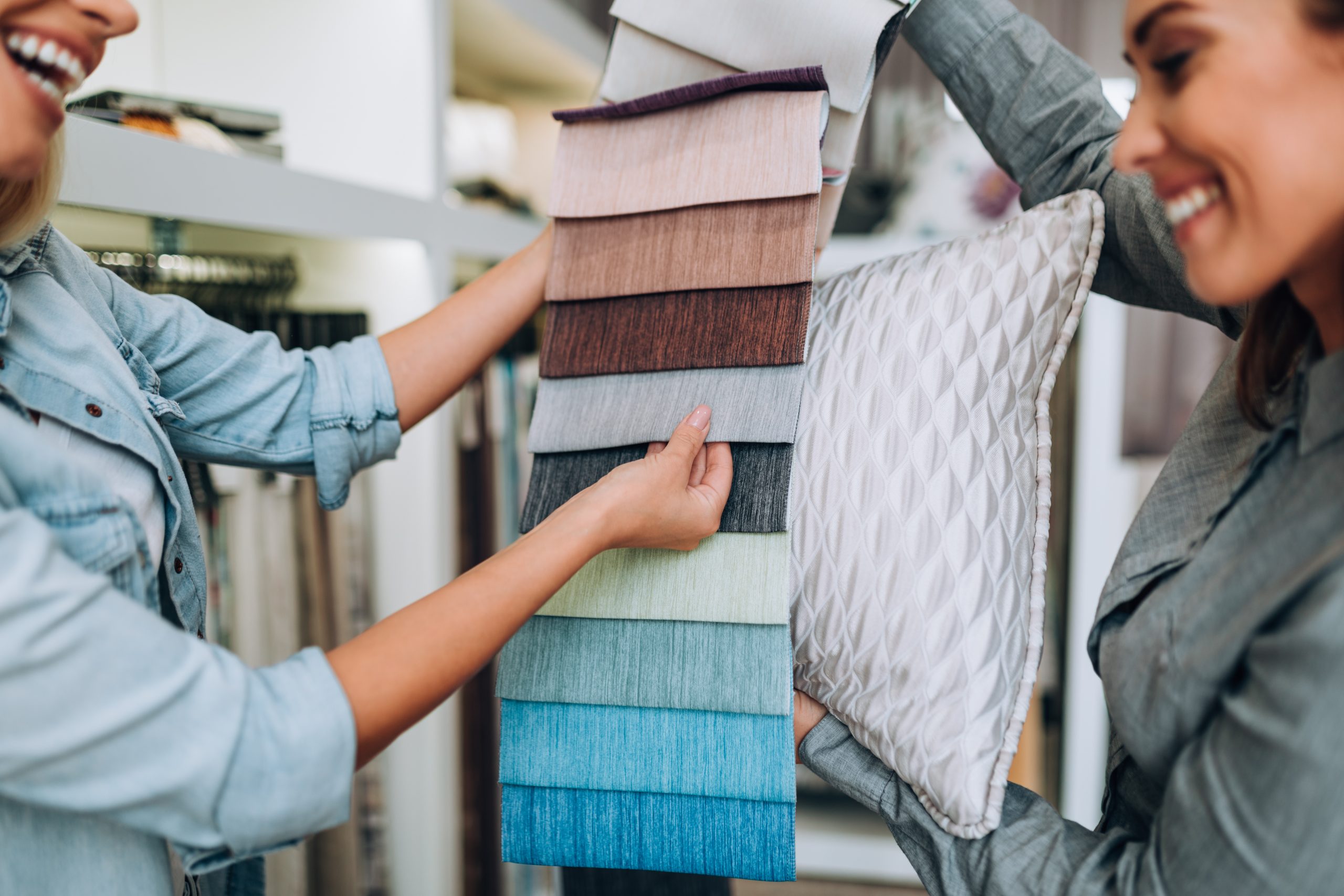 Young woman designer talking with a saleswoman and chooses fabrics for curtains in textile show room.